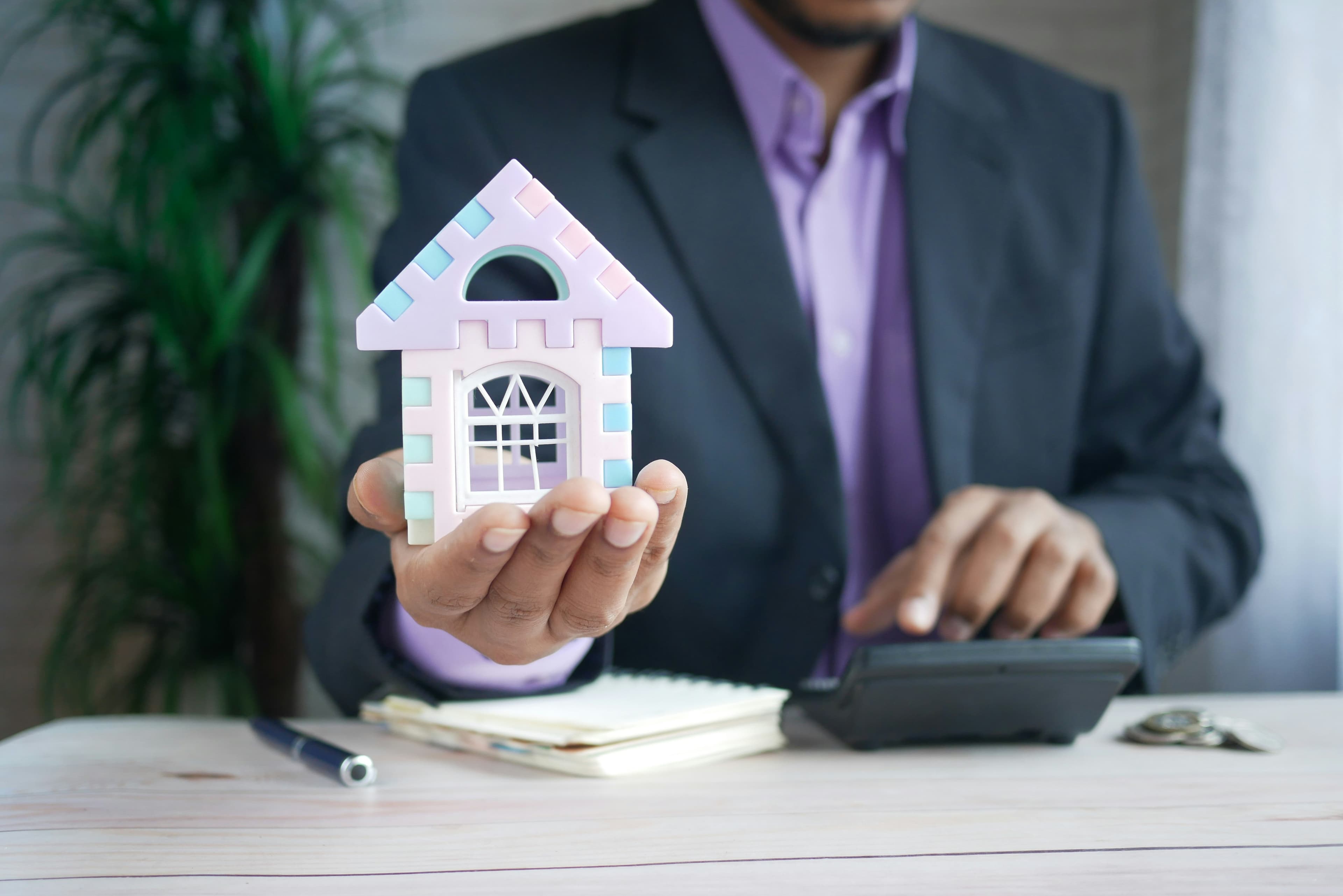 Property professional holding a model house beside a calculator